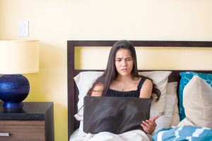 Beautiful biracial teen girl sitting in bed with laptop, making a surprised or disgusted expression
